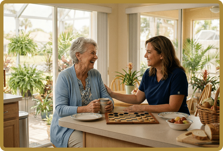 An elderly woman and a female caregiver share a laugh at a bright kitchen island while playing checkers and sipping tea.