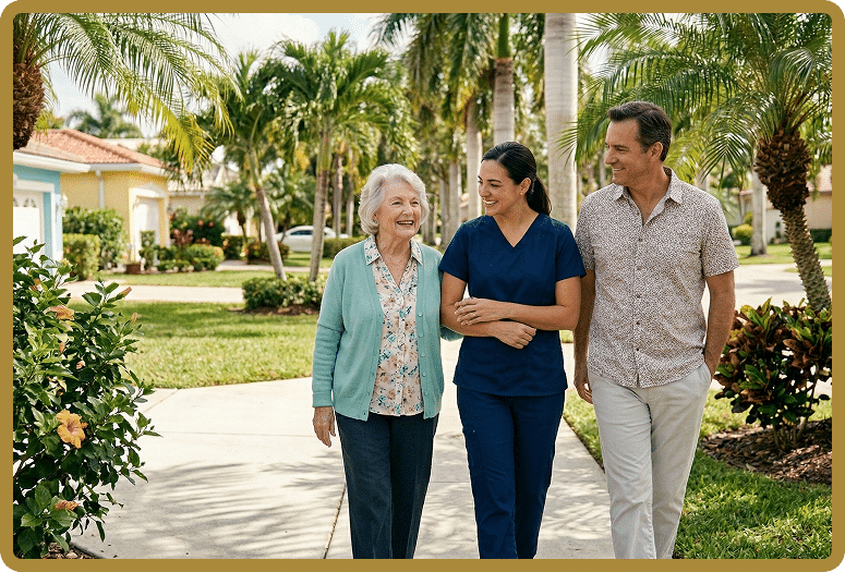 A nurse in navy scrubs walks arm-in-arm with an elderly woman and her husband down a sunny suburban sidewalk, palm trees in the background.